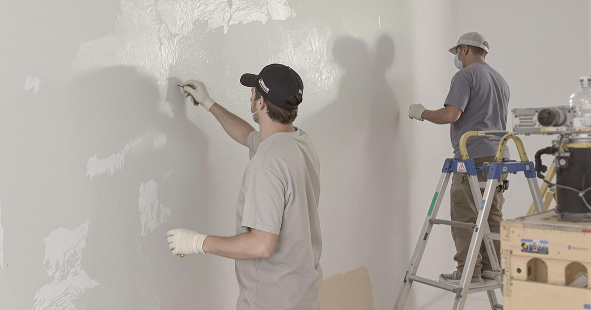 Projekt 367 zwei Arbeiter glätten und streichen eine Wand während der Renovierung.