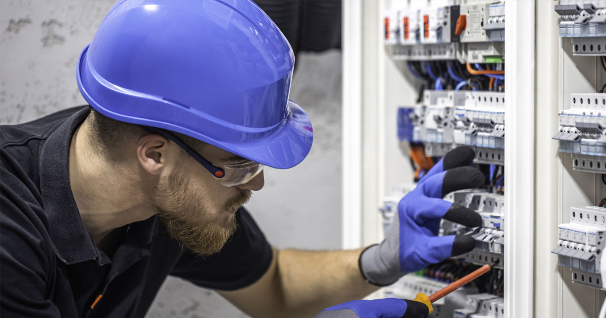 Projekt 372 zeigt einen Elektriker mit Schutzhelm bei der Arbeit an einem komplexen Sicherungskasten.